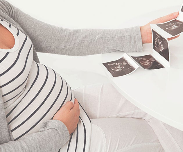 Pregnant mother holding her baby bump while looking at her ultrasound scan