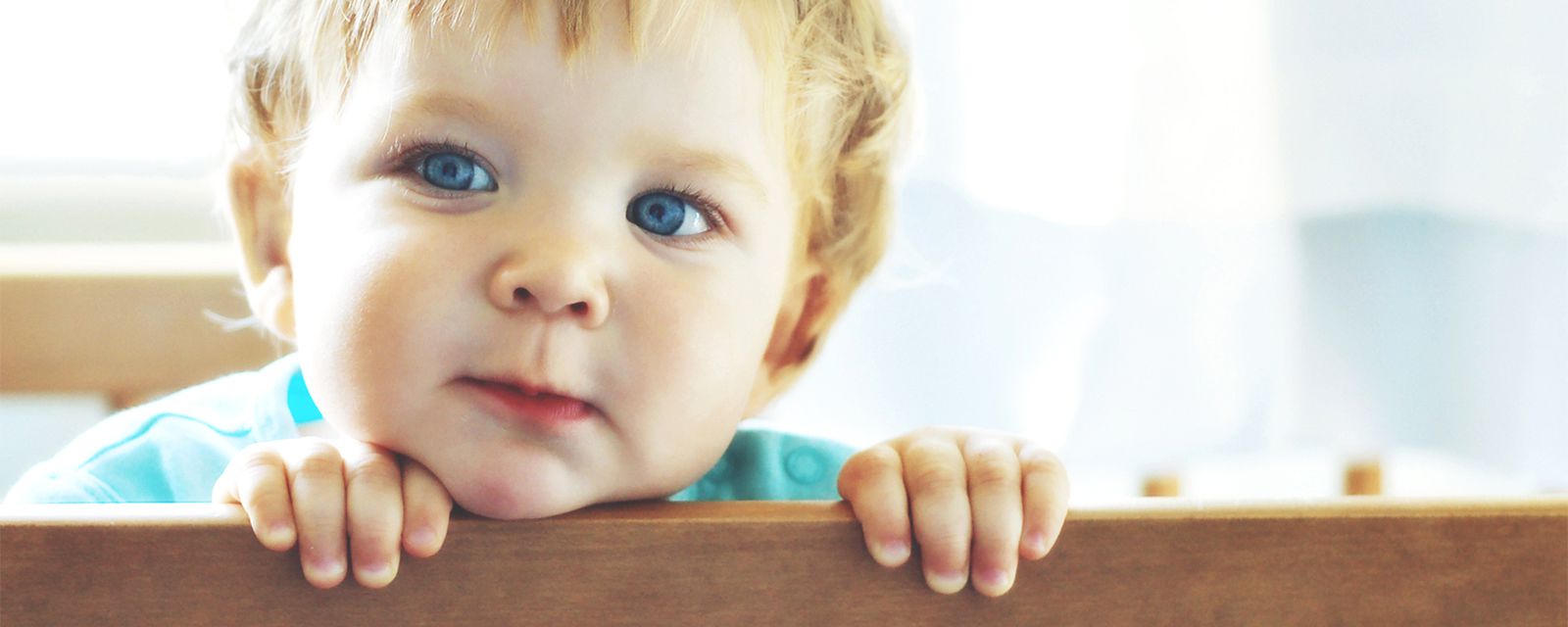 A baby looking over a bedframe