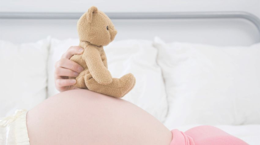 36 weeks pregnant mother holding a teddy bear on her pregnancy bump