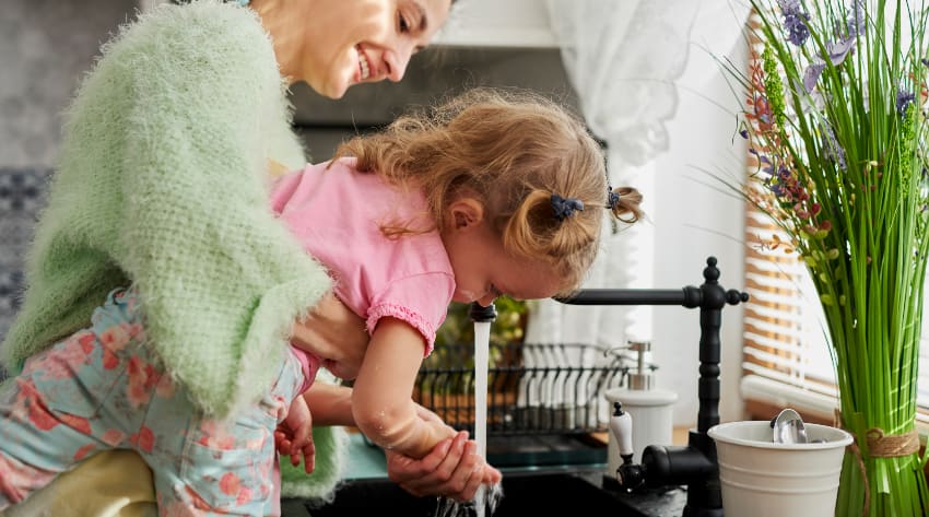 Mother and toddler daughter washing their hands in the kitchen sink