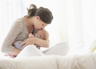 woman siting crossed legged while comforting and kissing a newborn on the forehead