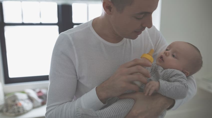 Man about to bottle feed a baby in his arms