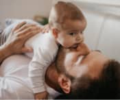 First time dad laying down and hugs newborn across his chest and giving kisses