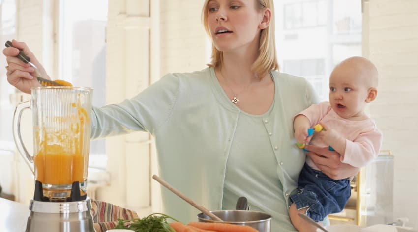 Mum preparing baby weaning food with baby in her arms