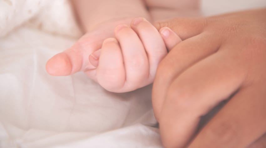 newborn baby holding onto mother’s finger