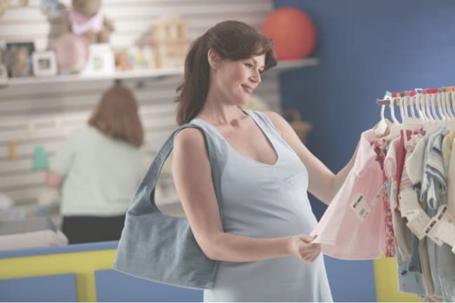 a pregnant woman looking at baby clothes