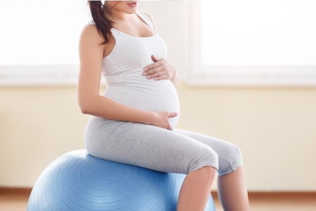 A Pregnant woman sitting on a medicine ball