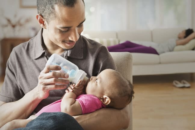 Caregiver feeding a baby with a bottle at home, showing formula milk preparation and storage