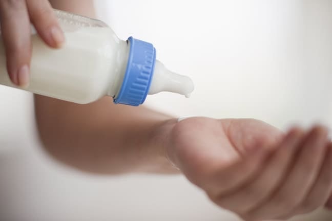 Formula milk from a baby bottle drips onto a hand to check the temperature before feeding