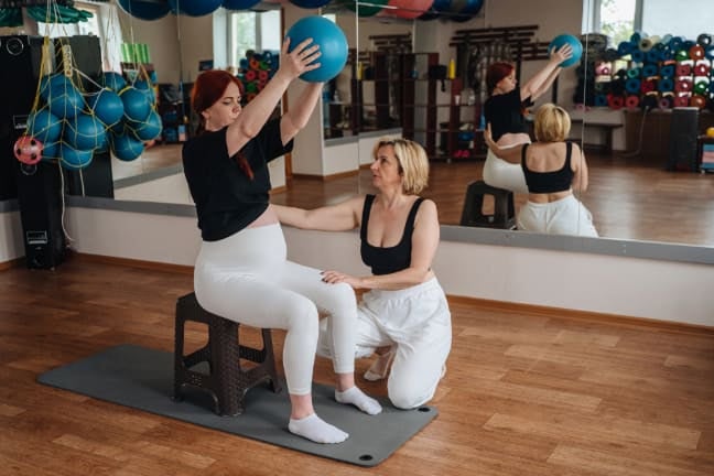 rtum exercise session with a fitness instructor helping a new mother perform a seated stability ball exercise for postnatal s