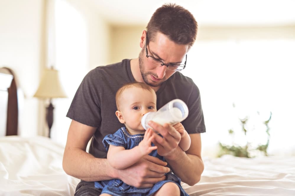 Infant drinking their usual milk from a bottle while being held by a caregiver during the weaning journey