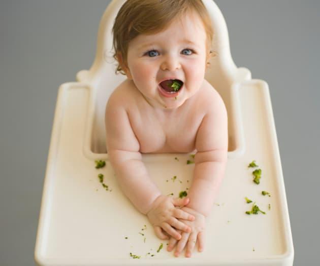 Baby sat on a baby-chair eating broccoli