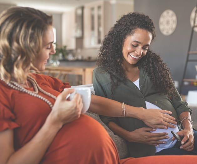 Two pregnant women socialising over a hot beverage.